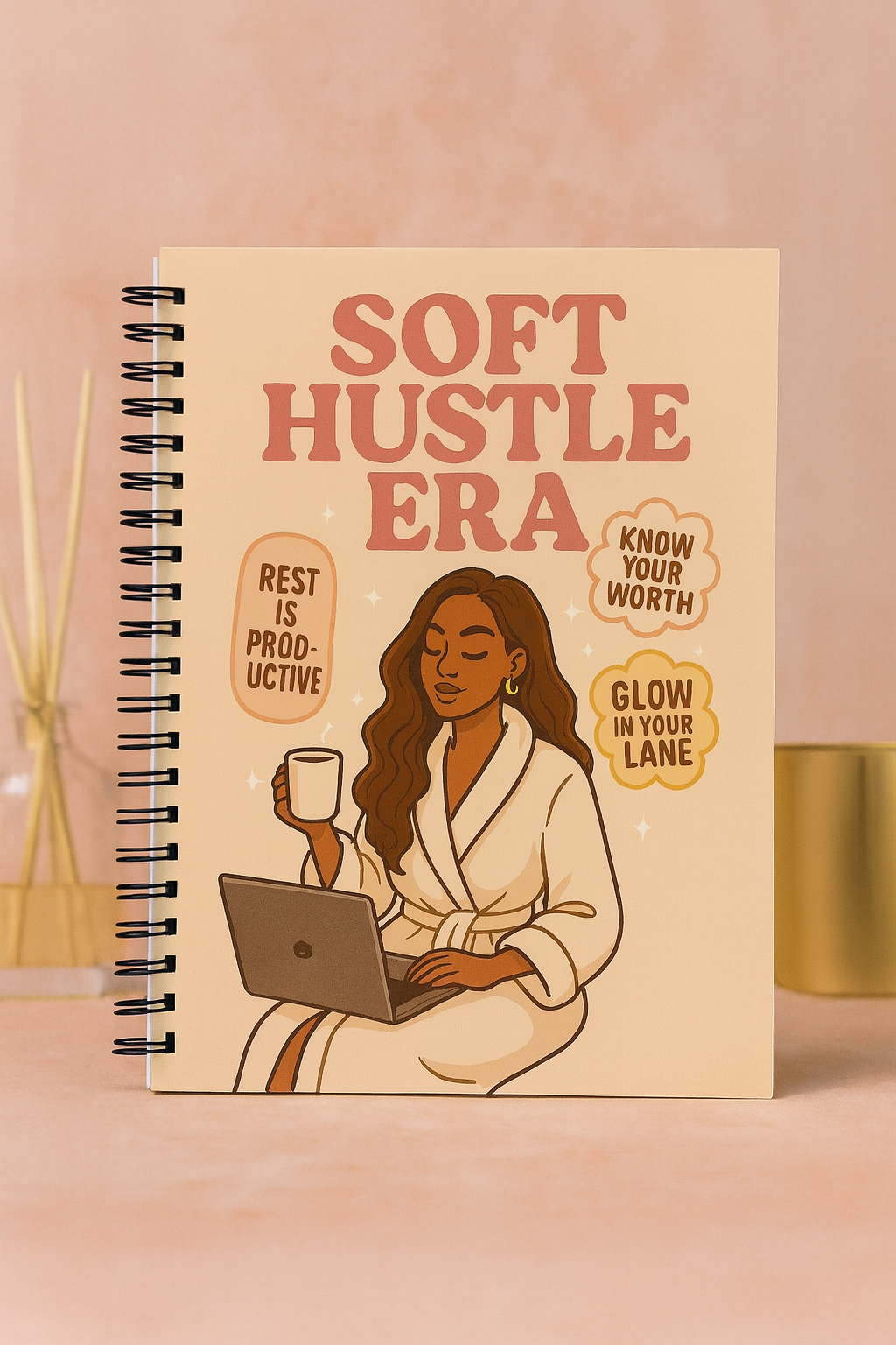 Cover of handmade spiral journal titled ‘Soft Hustle Era’ featuring a woman in a robe with coffee and laptop.