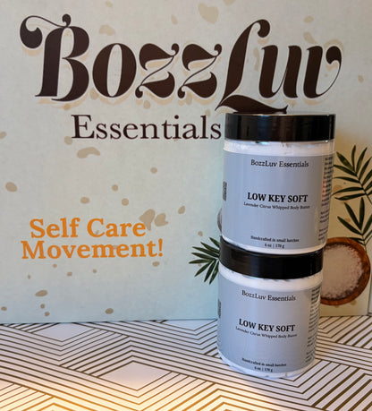 Two jars of BozzLuv Essentials Low Key Soft lavender citrus whipped body butter stacked on a patterned surface with branded backdrop
