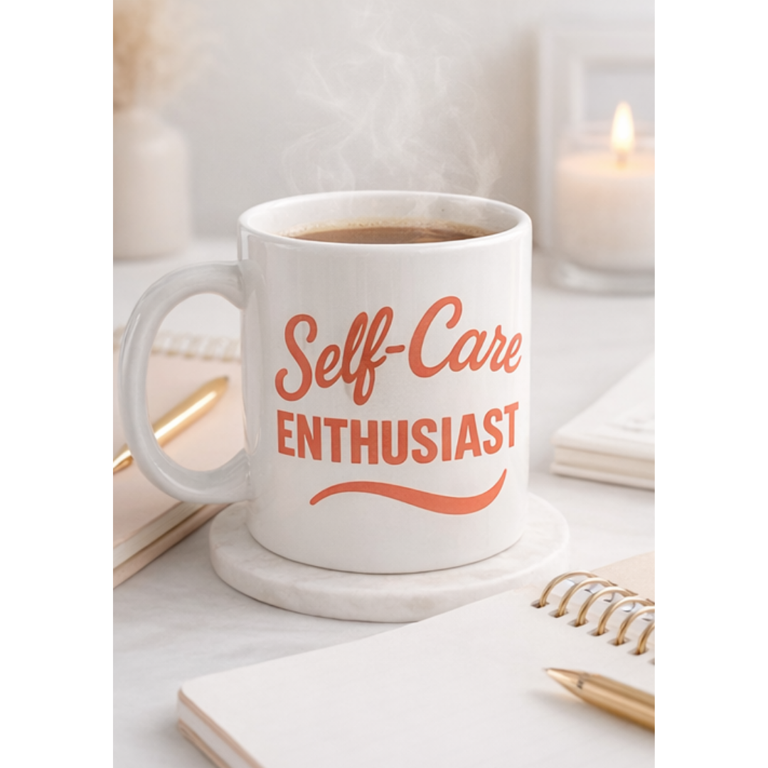White mug with 'Self-Care Enthusiast' text on a desk with a notebook and pen.