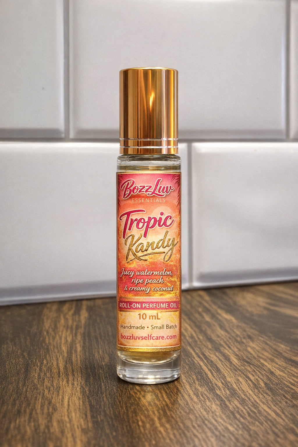 Roll-on perfume bottle labeled 'Tropic Kandy' by Bozz Luu on a wooden surface with a neutral background. BozzLuv Essentials Tropic Kandy roll-on perfume oil in a 10 mL glass bottle with gold cap and tropical label